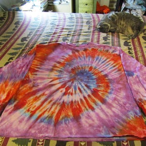 May include: A long-sleeved tie-dye shirt with a swirling pattern in shades of pink, orange, blue, and white.