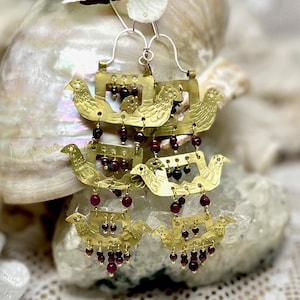 May include: Gold-toned metal earrings featuring bird designs and dangling red beads. The earrings have a layered design with multiple bird figures and small, round red beads hanging from the bottom. The earrings are displayed on a white surface.