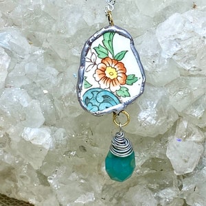 May include: A silver chain necklace with a pendant made from a vintage china plate featuring a floral design. The pendant is accented with a teal gemstone.