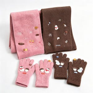 Puede incluir: Un conjunto de dos bufandas de punto y dos pares de guantes de punto en rosa y marrón. La bufanda y los guantes rosas presentan motivos invernales bordados como muñecos de nieve y bellotas. Las piezas marrones tienen diseños similares.