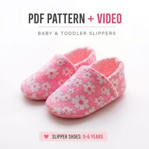 Może przedstawiać: Para różowych kapci dla niemowląt i małych dzieci w biały kwiatowy wzór. Tekst powyżej brzmi PDF PATTERN + VIDEO BABY & TODDLER SLIPPERS, a tekst poniżej brzmi SLIPPER SHOES: 0-6 YEARS z małą ikoną serca.