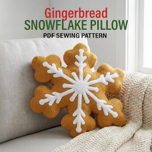 May include: A gingerbread-colored snowflake pillow with white accents rests on a light gray couch. The pillow is shaped like a snowflake with a white center and white details. Text above the pillow reads "Gingerbread Snowflake Pillow PDF Sewing Pattern."
