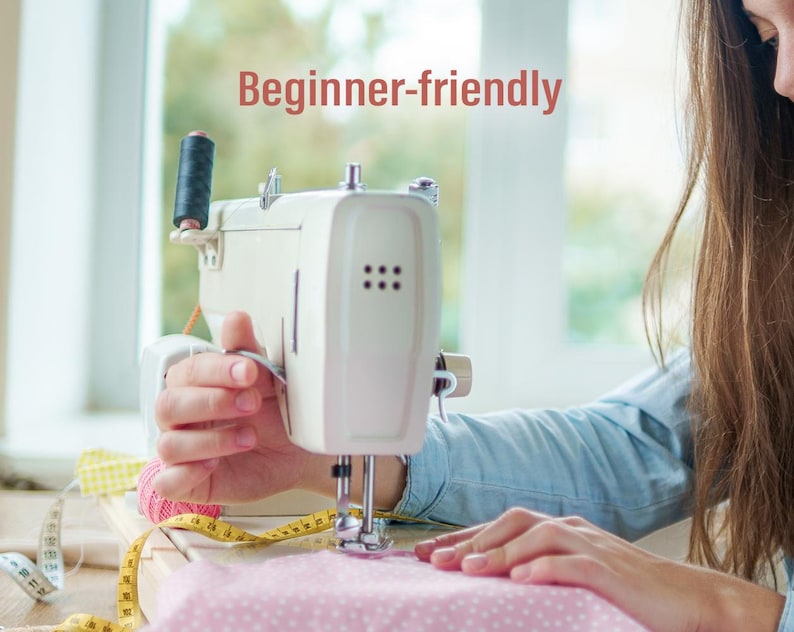 Peut inclure: Une machine &agrave; coudre blanche avec une bobine de fil noire est en cours d'utilisation. Elle coud un tissu rose &agrave; pois blancs. Un m&egrave;tre ruban jaune et du fil rose sont &eacute;galement visibles. Le texte "Beginner-friendly" est affich&eacute;.