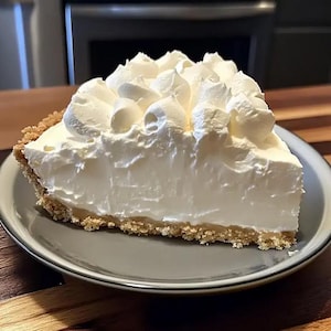 May include: A slice of pie on a grey plate. The pie features a biscuit crumb base, a white creamy filling, and is topped with whipped cream. The plate has a dark blue rim.