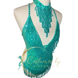 May include: Teal beaded halter top with fringe detail and matching beaded choker necklace. The top has a V-neckline and is made of sequins and beads. The choker is also made of sequins and beads and has a fringe detail. The top and choker are both very sparkly and glamorous.