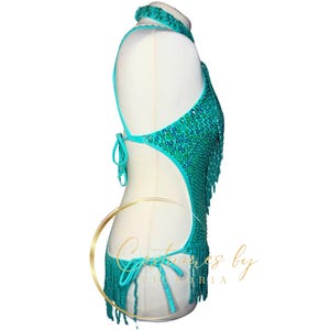 May include: A turquoise halter top with a beaded design and fringe. The top has a cutout back and is made of a stretchy fabric.
