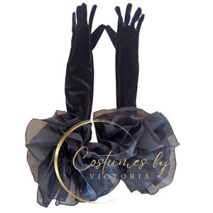 Può includere: Guanti da opera in velluto nero con finiture in organza a balze. I guanti sono lunghi, si estendono oltre il gomito e sono abbinati a un accento a balze coordinato. Il testo "Costumes by VICTORIA" è visibile.