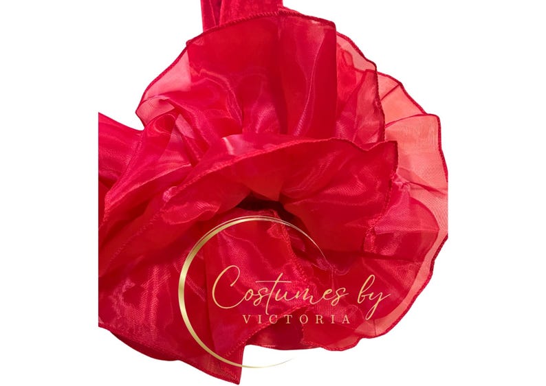 Pu&ograve; includere: Un tessuto di tulle rosso vivo con una texture arricciata. Il tessuto &egrave; raccolto in una forma circolare, creando un effetto voluminoso e drammatico. Il testo "Costumes by Victoria" &egrave; visibile al centro del tessuto.