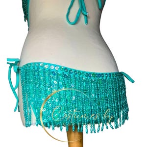 May include: Teal sequined and beaded fringe bikini bottom with a tie side. The fringe is made of small, round beads.