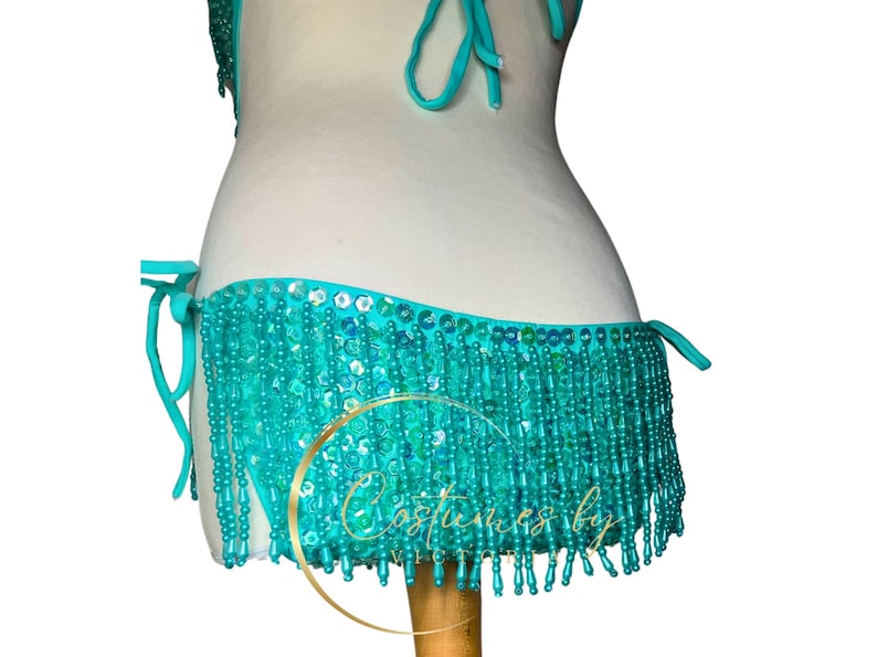 May include: Teal sequined and beaded fringe bikini bottom with a tie side. The fringe is made of small, round beads.