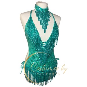 May include: Teal sequined halter top with fringe detail. The top has a deep V-neckline and is adorned with beads. The top is on a white mannequin.