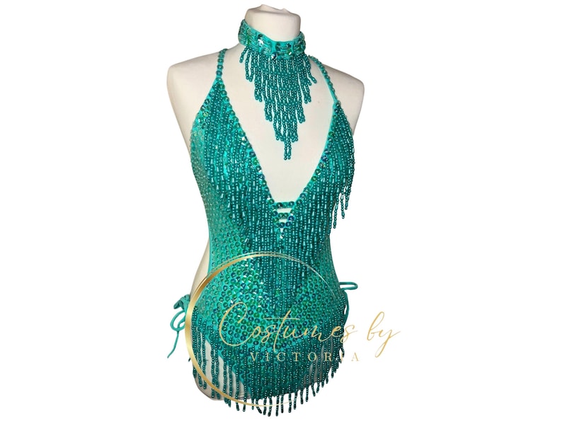 May include: Teal sequined halter top with fringe detail. The top has a deep V-neckline and is adorned with beads. The top is on a white mannequin.
