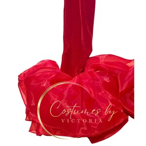 Pu&ograve; includere: Tessuto rosso trasparente in forma di balze e pieghe. Il tessuto &egrave; traslucido e ha una consistenza morbida e fluida. Il testo "Costumes by Victoria" &egrave; visibile al centro dell'immagine.