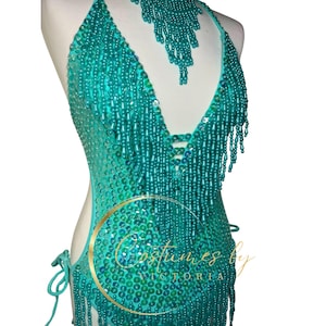 May include: A turquoise beaded halter top with fringe. The top is made of small, iridescent beads and has a deep V-neckline. The fringe is made of long strands of beads that hang down from the neckline.