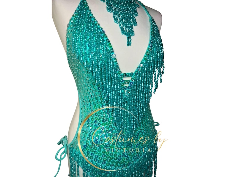 May include: A turquoise beaded halter top with fringe. The top is made of small, iridescent beads and has a deep V-neckline. The fringe is made of long strands of beads that hang down from the neckline.