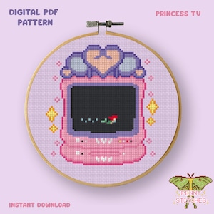Puede incluir: Un patrón de punto de cruz en un bastidor de madera con un diseño de pixel art de una consola de juegos portátil rosa con una forma de corazón en la parte superior. La pantalla muestra una pequeña figura roja y verde. Texto DIGITAL PDF PATTERN PRINCESS TV.