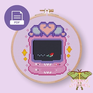 Può includere: Un motivo a punto croce in un telaio da ricamo in legno raffigurante una console portatile rosa con una parte superiore a forma di cuore. Lo schermo mostra una piccola sirena. Lo sfondo è viola chiaro con stelle gialle e un'icona PDF.