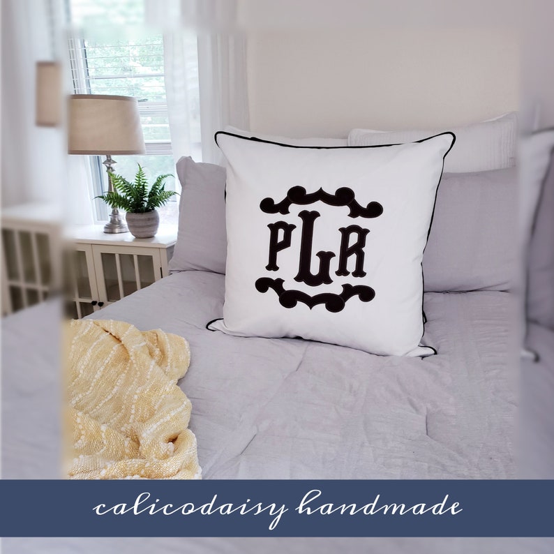 May include: White pillow with black embroidered monogram "PLR" in a decorative frame. The pillow has a black piping trim and is on a bed with a white and gray quilt.