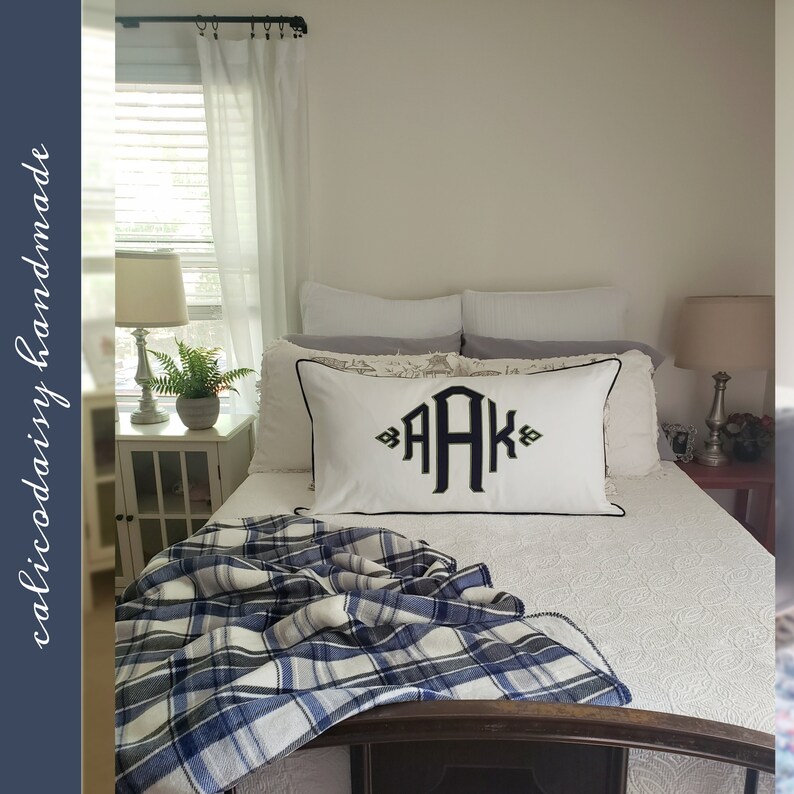 May include: A white bed with a blue and white plaid throw blanket. The bed has a white pillow with black embroidery that says "AAK".