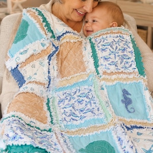 May include: A handmade rag quilt featuring a patchwork of square fabric panels in shades of blue, teal, and tan. The quilt displays various nautical prints including seahorses, starfish, seashells, and sea turtles with frayed seams.