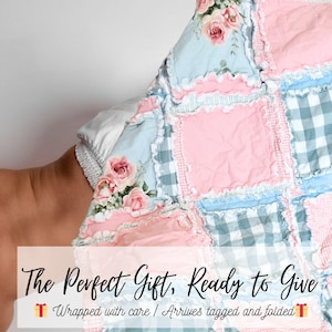 May include: A patchwork rag quilt featuring alternating squares of light blue fabric with pink rose floral patterns, solid light pink fabric, and light blue and white gingham check fabric, all joined with exposed frayed seams and decorative stitching.