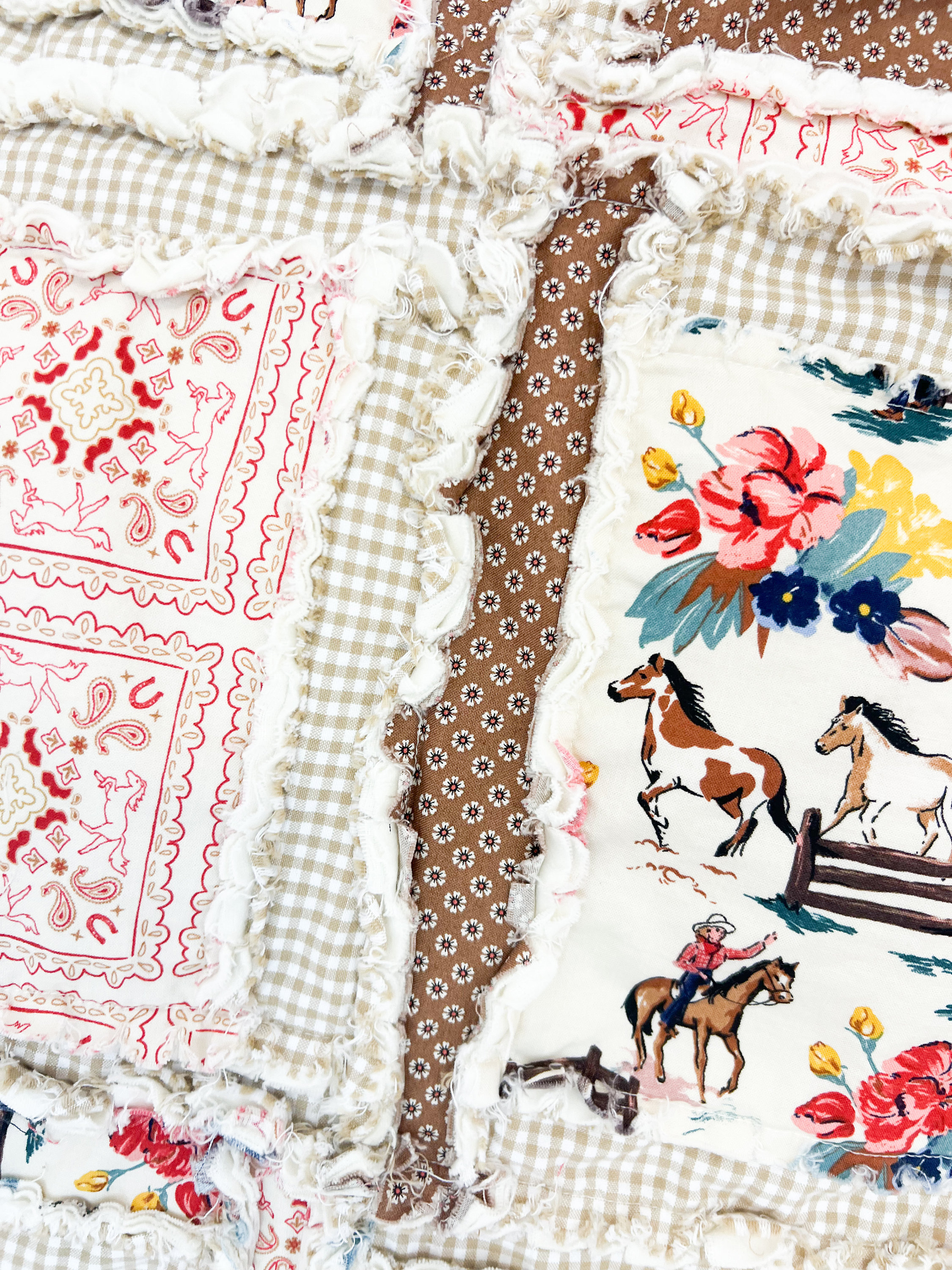 May include: A patchwork quilt with a variety of fabrics, including gingham, paisley, and floral prints. The quilt features a brown and white gingham pattern, a red and white paisley pattern, and a white floral pattern with horses and cowboys. The quilt is made with a frayed edge.