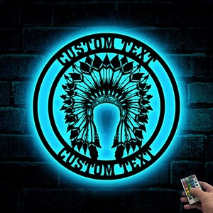 May include: A blue neon light with a black silhouette of a Native American headdress. The light has a circular shape with the words "CUSTOM TEXT" written around the edge.