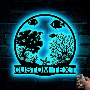 May include: A blue neon sign with a circular design featuring silhouettes of coral, fish, and a starfish. The sign has a customizable text area that reads "CUSTOM TEXT".