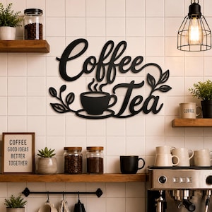 Könnte beinhalten: Ein schwarzes Metall-Wandschild mit den Wörtern Coffee und Tea in Schreibschrift, ergänzt durch ein zentrales Tassen- und Untertassen-Symbol sowie dekorative Blattmotive an beiden Seiten, montiert an einer weißen Fliesenwand.