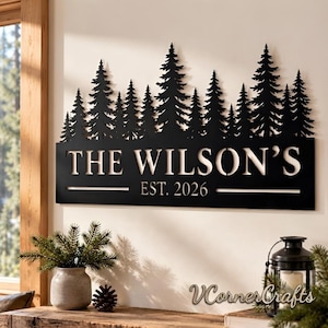 May include: A black metal wall sign featuring a silhouette of a pine forest along the top edge. The text reads THE WILSON'S and EST. 2026 in a clean, sans-serif font. The design is rectangular with a flat base and a jagged, tree-lined top border.
