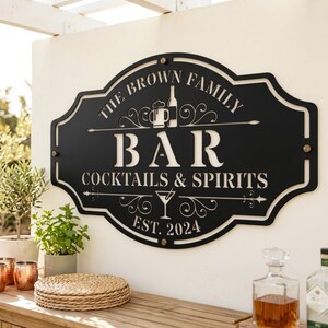 May include: A black metal wall sign with a decorative scalloped edge featuring the text THE BROWN FAMILY, BAR, COCKTAILS & SPIRITS, and EST. 2024. The design includes cut-out icons of a beer mug, a wine bottle, and a martini glass with swirls.
