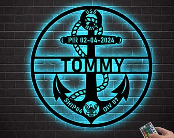 May include: A black metal anchor with a personalized name "TOMMY" and the text "USS NAVY PIR 02-04-2024 SHIP 04 DIV 07" in a circle. The anchor is illuminated with a blue light.