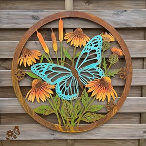 May include: A circular metal wall art piece featuring a large, bright blue butterfly centred among orange coneflowers, green leaves, and tall cattails. The entire design is enclosed within a rusted, weathered brown circular metal frame.
