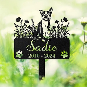 以下が含まれることがあります： 黒い金属製のガーデンステーク。ボストンテリアのデザイン、名前「Sadie」、2010年から2024年。足跡と花の装飾が含まれており、ペットの記念に最適です。