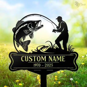 May include: Black metal silhouette of a fisherman holding a fishing rod with a large fish jumping out of the water. The sign has a black banner with the text "CUSTOM NAME 1970 - 2025".