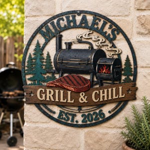 May include: A circular metal wall sign featuring a black smoker grill, a red steak, and green pine trees. The text reads "MICHAEL'S", "GRILL & CHILL", and "EST. 2026". The design includes a wood-textured banner across the centre and a blue-toned border.