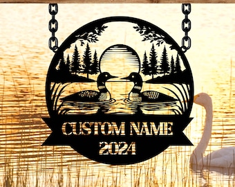 May include: Black metal silhouette of two loons facing each other on a lake with trees and a sun in the background. The text "CUSTOM NAME 2024" is below the loons.