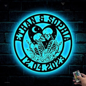 May include: A black metal sign with the text "Ethan & Sophia 12.04.2023" and a design of two skeletons embracing inside a heart.
