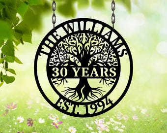 Könnte beinhalten: Schwarzes Metallschild mit der Aufschrift "THE WILLIAMS", einem Baumdesign und dem Text "30 YEARS EST. 1994". Das Schild hängt an Ketten. Der Hintergrund ist verschwommen mit grünen Blättern und Blumen.