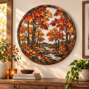 May include: A circular wall art piece featuring a layered wooden landscape of autumn trees with vibrant red, orange, and yellow maple leaves. The scene depicts a flowing stream, rocky terrain, and distant mountains enclosed in a dark wood frame.