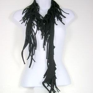 May include: A black fringed scarf made of soft fabric. The scarf is long and narrow, with a frayed edge. It is draped over a white mannequin.