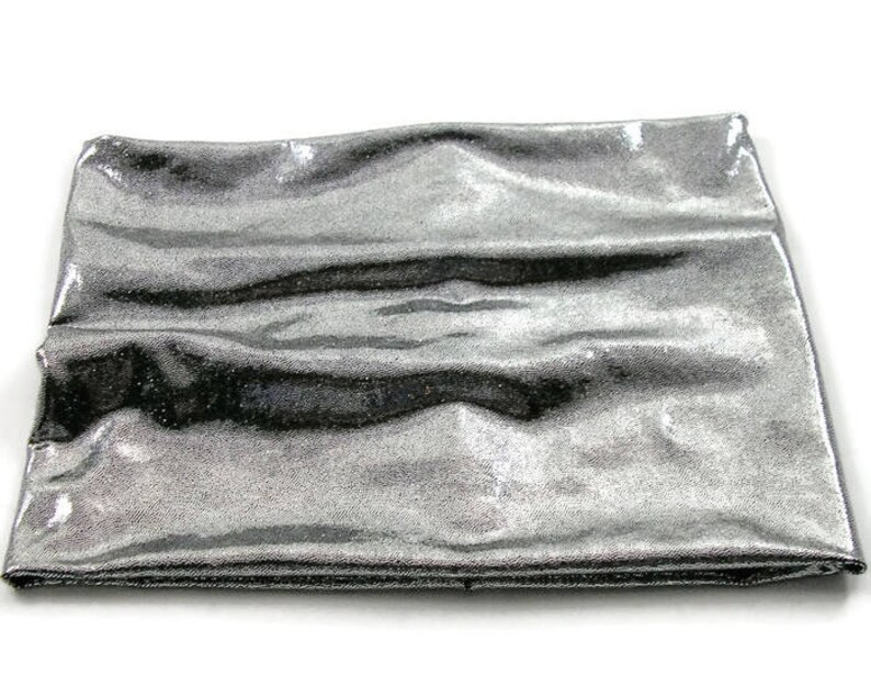May include: A silver metallic fabric with a smooth, shiny texture. The fabric is folded and appears to be soft and flexible.