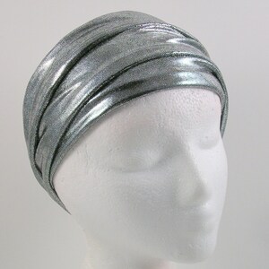 May include: A silver metallic turban headband with a shiny, textured finish. The headband is folded and wrapped around a white mannequin head.
