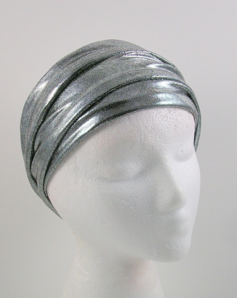 May include: A silver metallic turban headband with a shiny, textured finish. The headband is folded and wrapped around a white mannequin head.