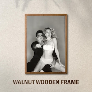 Peut inclure: Tirage encadr&eacute; en noir et blanc d'un homme et d'une femme dans une pose suggestive. La femme porte un haut et un bas blancs. L'homme pointe du doigt. Le cadre est en noyer. Le texte "WALNUT WOODEN FRAME" est en bas.