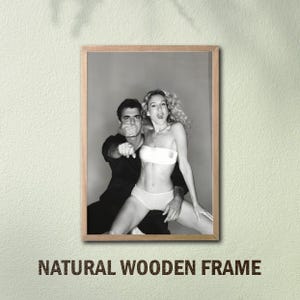 Peut inclure: Tirage encadr&eacute; en noir et blanc repr&eacute;sentant un homme et une femme. L'homme couvre la bouche de la femme et pointe. La femme porte un haut et un sous-v&ecirc;tement blancs. Le cadre est en bois naturel. Texte : "NATURAL WOODEN FRAME".