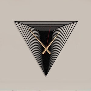 Puede incluir: Un reloj de pared geométrico negro en forma de triángulo, con manecillas doradas y un segundero rojo. El reloj está montado en una pared clara sobre una cama. El diseño crea una ilusión óptica de profundidad.
