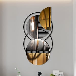May include: A black metal wall decor featuring three overlapping circles. The circles are made of black metal and have a gold mirror finish. The decor is hanging on a white wall in a modern living room.