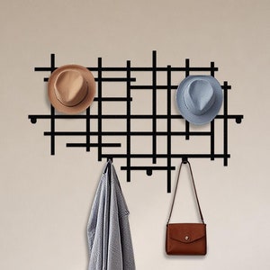 May include: Black metal wall-mounted grid with hooks for hanging items. Two hats, a handbag, and a piece of clothing are hanging on the hooks.