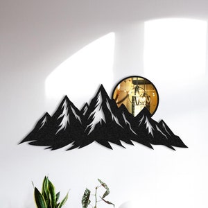May include: Black metal mountain range wall decor with a round mirror in the shape of a sun. The decor is mounted on a white wall above a wooden cabinet and a gray armchair.